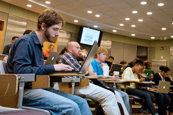 Photo of a Chatham University student sitting in a 查塔姆东区 lecture hall taking notes on his laptop.
